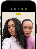 ブラックのiPhone 18 Pro、前面の外観。カメラに向かってポーズをとる2人のモデルが表示され、センターフレームフロントカメラの機能を示している