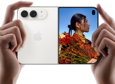 スターホワイトのiPhone Duo。横向きに開いた状態、両手で持っている。左側のパネルには48MP Dual Fusionバックカメラ、右側のパネルには写真を撮られている人物が映ったアウターディスプレイが見えている。写真の被写体は、Duo Previewを使って撮影されている自分の顔を見ることができる