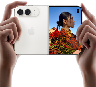 スターホワイトのiPhone Duo。横向きに開いた状態、両手で持っている。左側のパネルには48MP Dual Fusionバックカメラ、右側のパネルには写真を撮られている人物が映ったアウターディスプレイが見えている。写真の被写体は、Duo Previewを使って撮影されている自分の顔を見ることができる