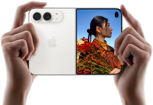 スターホワイトのiPhone Duo。横向きに開いた状態、両手で持っている。左側のパネルには48MP Dual Fusionバックカメラ、右側のパネルには写真を撮られている人物が映ったアウターディスプレイが見えている。写真の被写体は、Duo Previewを使って撮影されている自分の顔を見ることができる