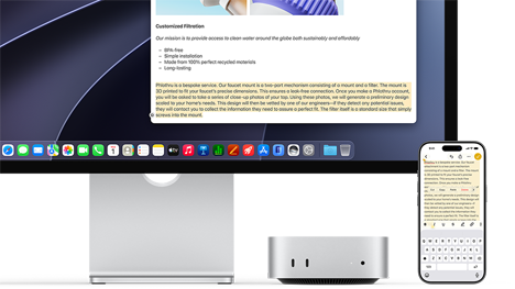 Studio Displayの下に収納されたMac miniの前面。Mac miniとStudio Displayの右側にiPhoneが置かれている。iPhoneの画面の上部でテキストが選択され、カット、コピー、ペースト、自動入力コマンドが表示されている。Studio Display上でも同じテキストがハイライトされており、ユニバーサルクリップボードを使っている様子を示している