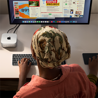 デスクでMac miniを使ってタイピングしている人物。Studio Displayが接続されている。Magic Keyboard、Magic Trackpad、様々なアイテムがある