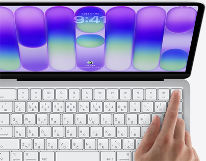 シルバーのMacBook Neo。ログイン画面が表示されていて、キーボードの右上角にあるTouch IDセンサーの上に指が置かれている